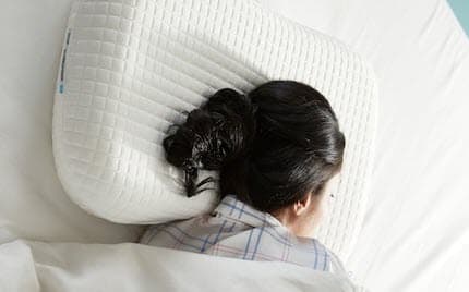 A young woman, laying on his side, is sleeping deeply on IKEA PRAKTVÄDD ergonomic pillow.