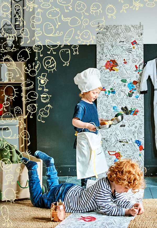 Duas crianças a brincar, uma delas vestida de cozinheiro e outra a colorir no chão