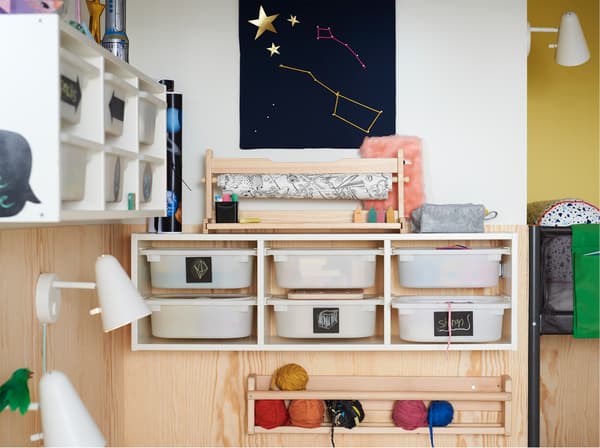 Aan de wand gemonteerde IKEA TROFAST opbergcombinatie voor speelgoed met zes lades met zwarte handgeschreven etiketten.