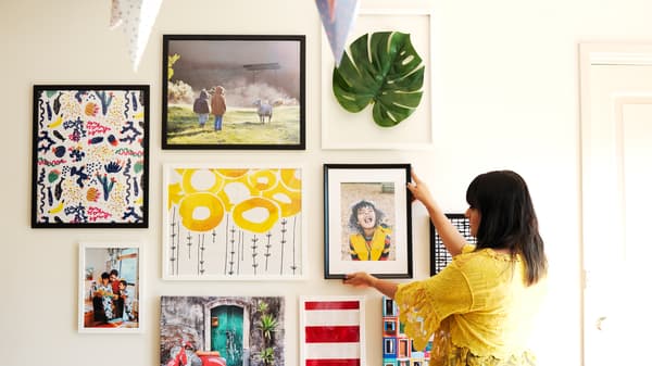 Abeer placing a framed photograph on a gallery wall to show to arrange a gallery wall of photos and artwork at home.