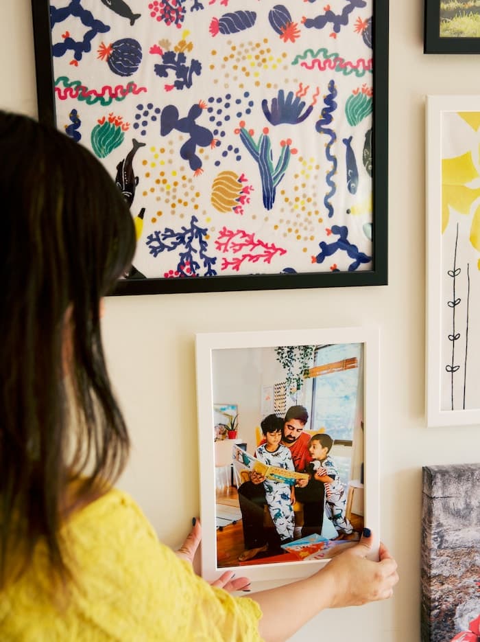 Abeer positioning a family photo on a gallery wall of pictures, using family photos to personalise a gallery wall.