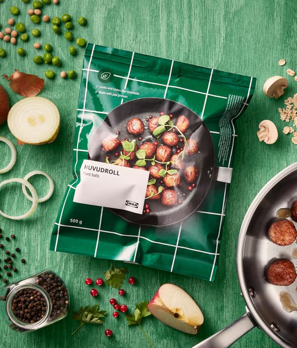 عبوة من الكرات النباتية HUVUDROLL من ايكيا موضوعة على سطح خشبي أخضر. العبوة محاطة بمكونات مختلفة.