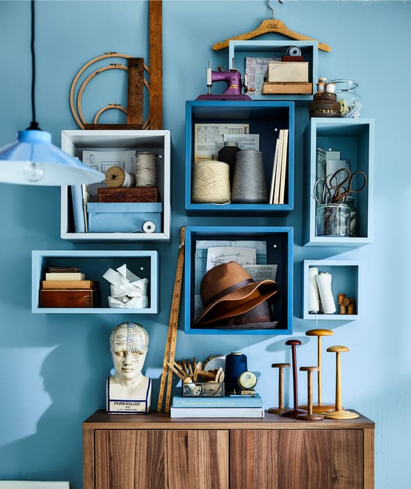 Accesorios de costura e libros almacenados en cubos brancos cunha parede azul de fondo.
