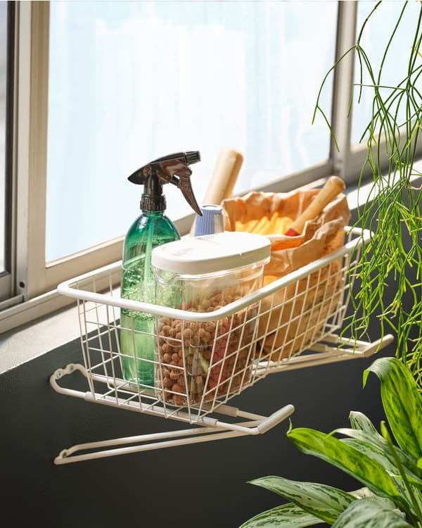 Accessoires de jardinage dans une corbeille en fil posée sur des crochets SKRÄLL fixés sous les fenêtres d’un balcon fermé.