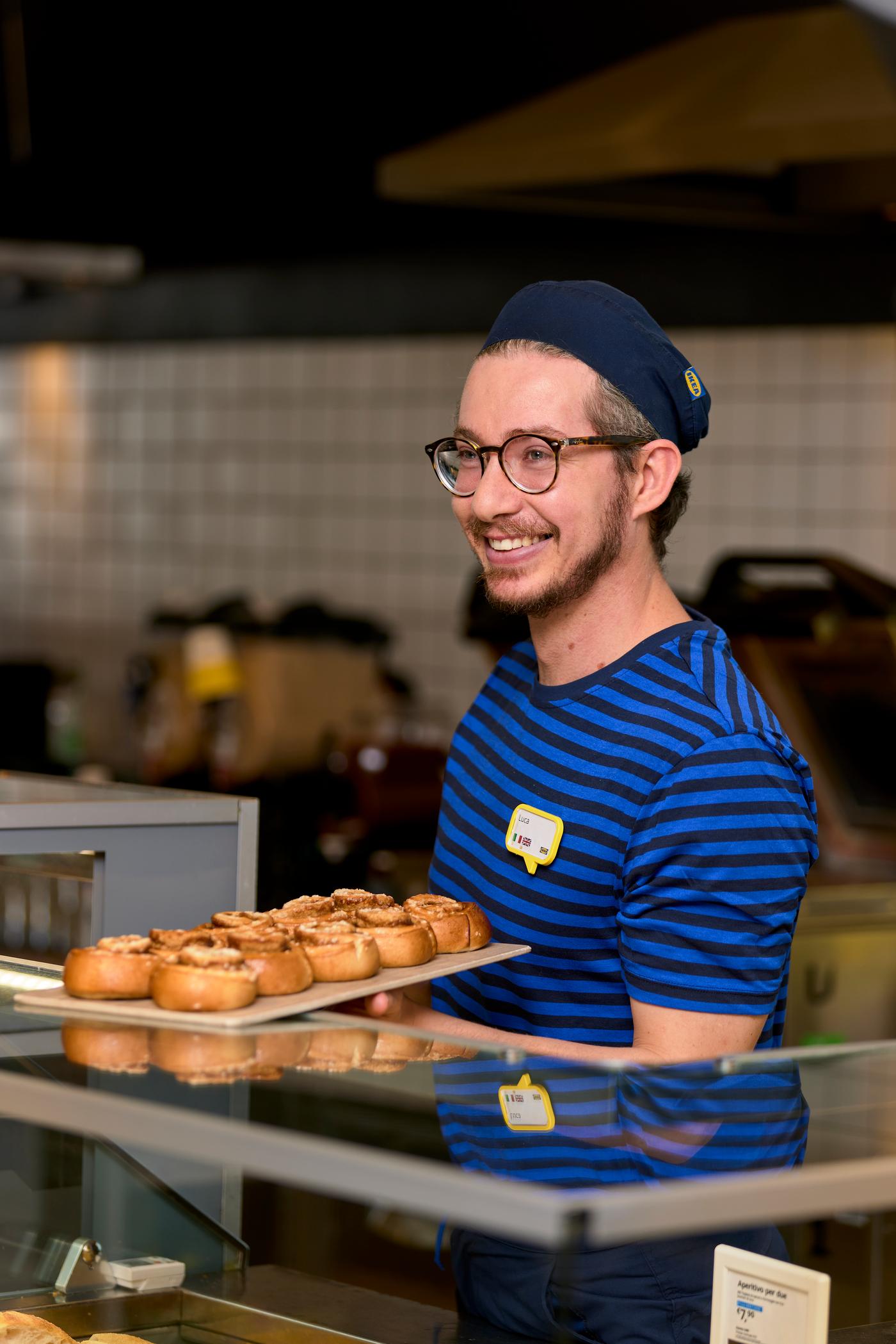 Addetto alla ristorazione  e al bar IKEA mentre appoggia sul bancone un vassoio pieno di dolci.