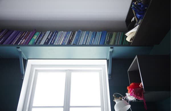 Additional storage for books, created using a shelf mounted on a large bedroom window.