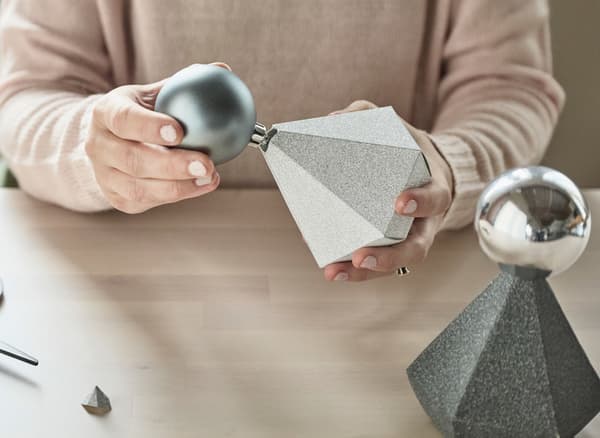 Adornos grises e prateados inseríndose na parte superior de caixas de papel en forma de diamante.