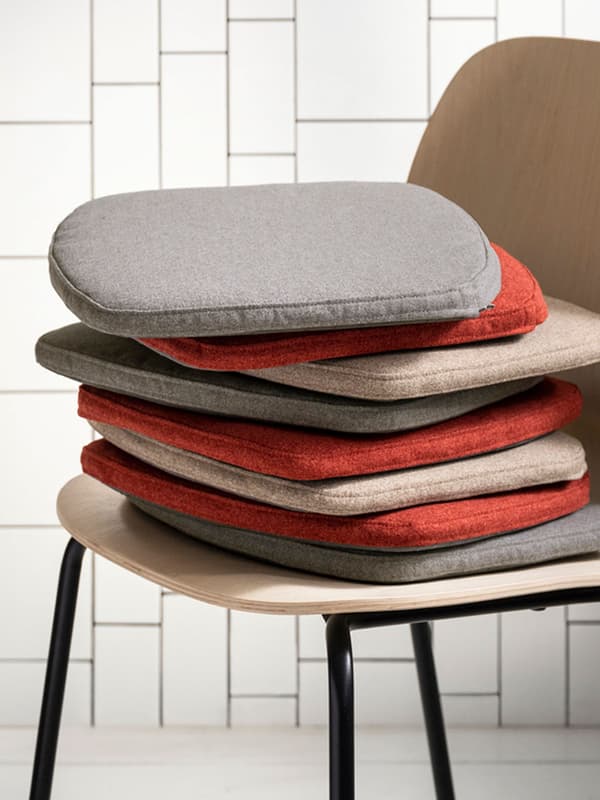 ÄLVGRÄSMAL chair pads in grey, red and beige are stacked on top of one another and placed on a beige chair.