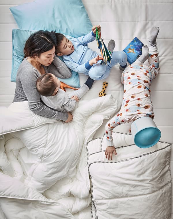 Aerial view of a mother and three children in bed reading DJUNGELSKOG  picture book and playing about under duvets.