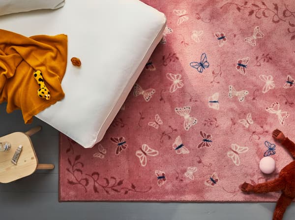 Aerial view of an IKEA SÅNGLÄRKA butterfly pink low pile rug, partially under a white chaise longue.