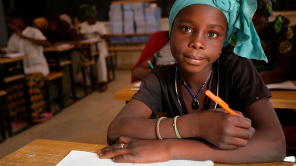 Africká dívka sedící ve škole v lavici s perem a sešitem.