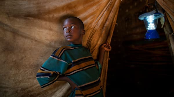 Africký chlapec stojí před přístřeškem v uprchlickém táboře.
