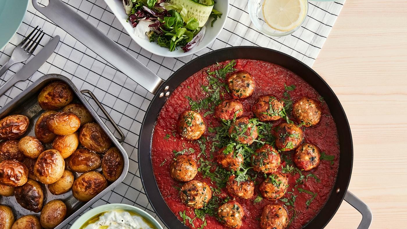 Albóndigas de proteína vegetal en una sartén, hechas con carne picada vegetal VÄRLDSKLOK y salsa de tomate, junto a una bandeja de patatas asadas.