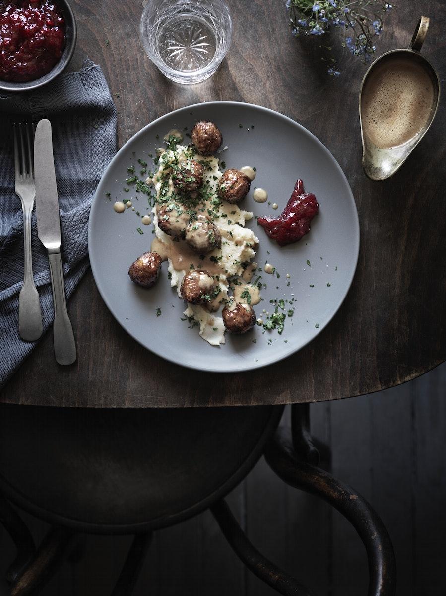 Albóndigas IKEA, arándanos rojos, salsa cremosa y puré de papas, servido sobre un plato blanco redondo. 