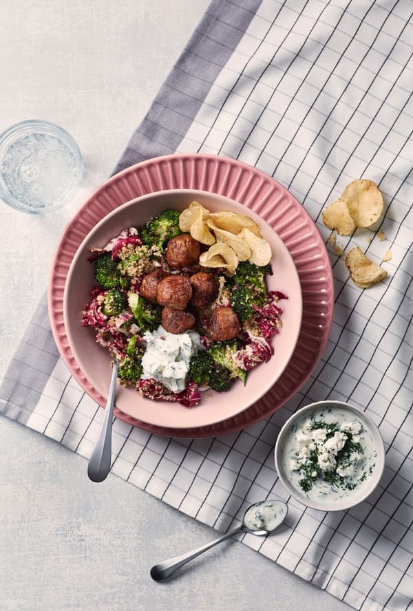 Albóndigas vegetales con ensalada de quinoa en un bowl rosado sobre un plato rosado más oscuro, sobre un individual blanco y gris a cuadros.