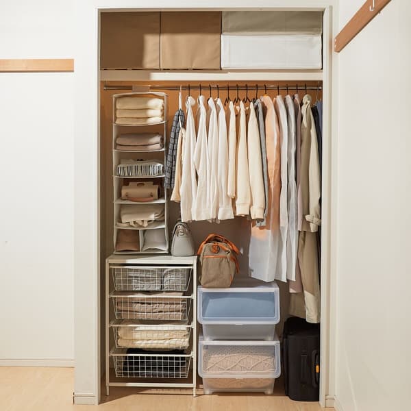 Alcuni abiti e borse sono riposti in ordine all'interno di una cabina armadio tramite appenditutto, grucce o cassetti. All'interno della cabina armadio ci sono un portatutto a 7 scomparti STUK, una combinazione di mobili JONAXEL, contenitori trasparenti, custodie SKUBB e scatole beige.