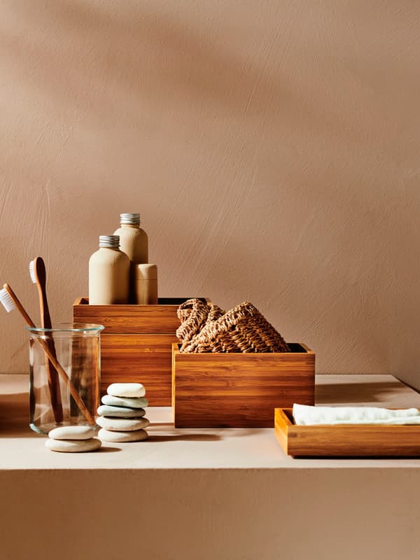 Alcuni accessori da bagno come saponi, spazzolini, creme e dispenser poste in contenitori e vassoi in legno.