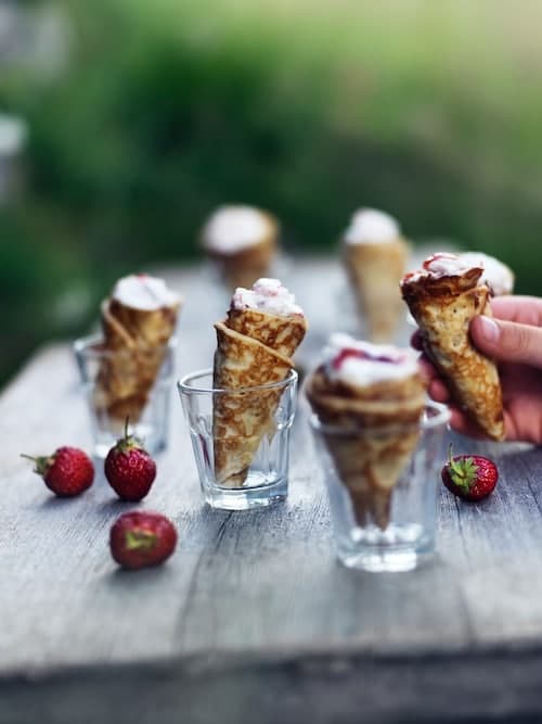 Alcuni finger food in bicchieri con attorno fragole. Una mano sta prendendo un dolcetto.