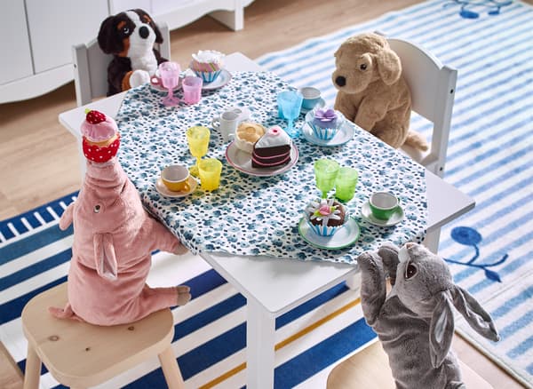 Alcuni peluche intorno a un tavolino con un servizio da tè giocattolo.