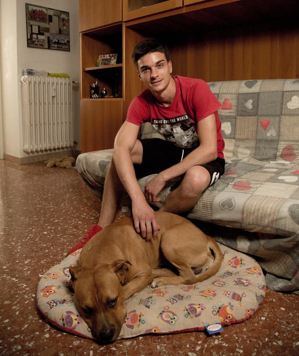 Alessandro นั่งอยู่บนโซฟาและมีสุนัขนอนอยู่บนที่นอนของมันข้างหน้าเขา