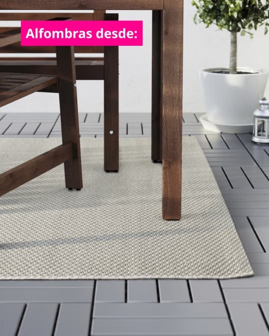 Alfombra exterior clara bajo una mesa de madera en una terraza, con superficie textil resistente y diseño simple. Texto en imagen dice: “Alfombras desde:”.