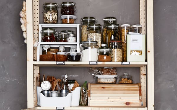 Aliments secs et épices conservés dans des bocaux en verre transparent sur une étagère en pin, dans des boîtes en plastique blanc.