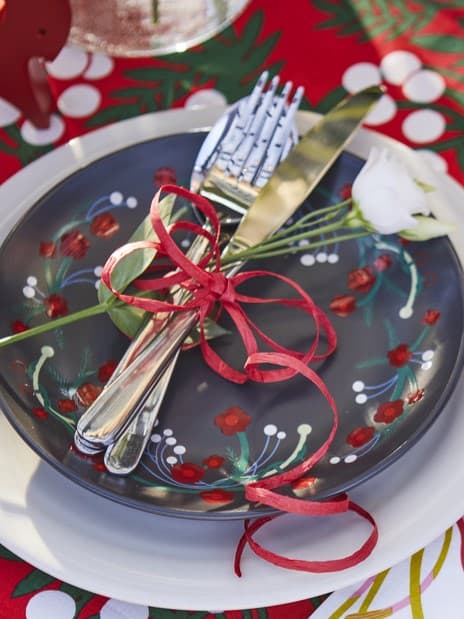 Allestimento di una tavola in stile natalizio con decorazioni e stoviglie VINTERFINT. Le posate sono legate con dei fiocchi a mo' di segnaposto.