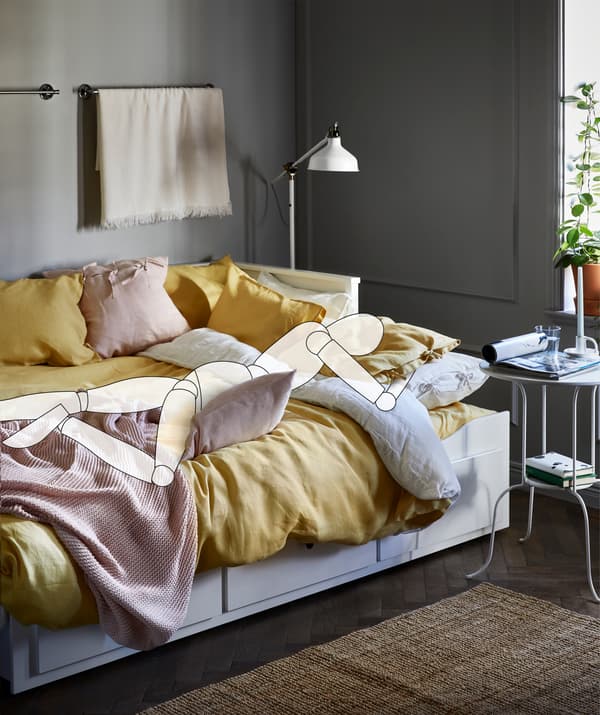 Allongée sur son ventre dans un lit rempli de textiles et de coussins, une silhouette tient un oreiller.