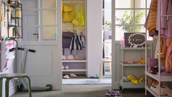 Almari pakaian VIHALS berwarna putih terletak di sebelah rak kot dengan storan kasut MACKAPÄR berwarna putih yang mempunyai kasut dan beg berwarna-warni di ruang depan yang disinari cahaya matahari.