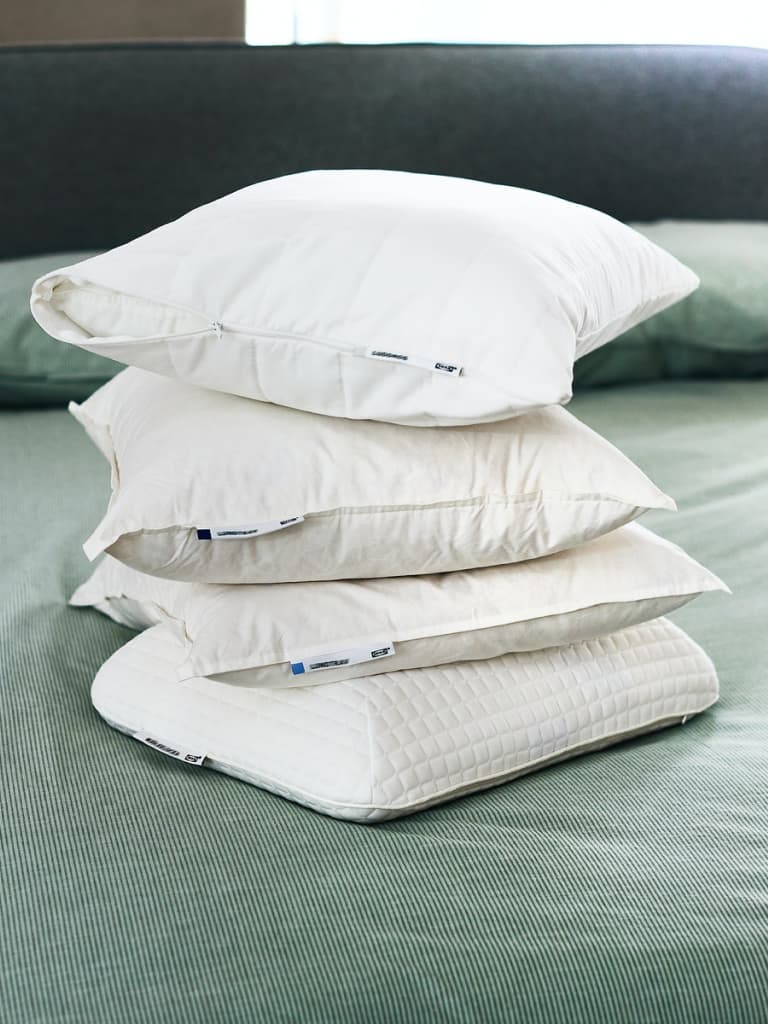 Almofada alta LUNDTRAV sobre um edredão e uma almofada com capa e roupa de cama SPIKVALLMO em azul e branco.