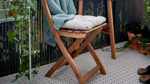 ALTAPPEN floor decking covers the floor of a balcony furnished with an ASKHOLMEN folding chair and table and plants.