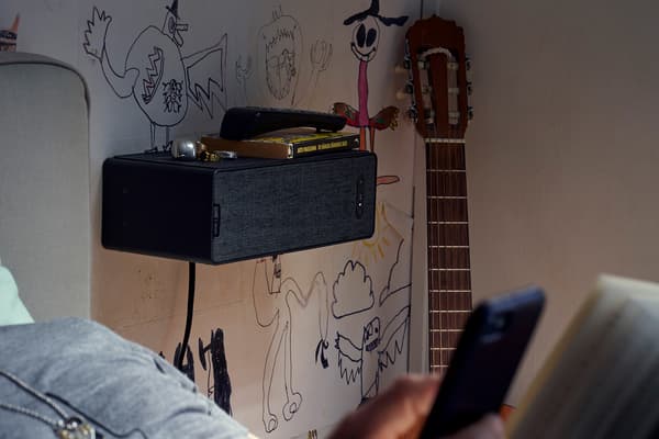 Altofalante estante SYMFONISK nunha parede dun dormitorio decorada con graffiti, cunha guitarra ao lado e unha cama en primeiro plano.