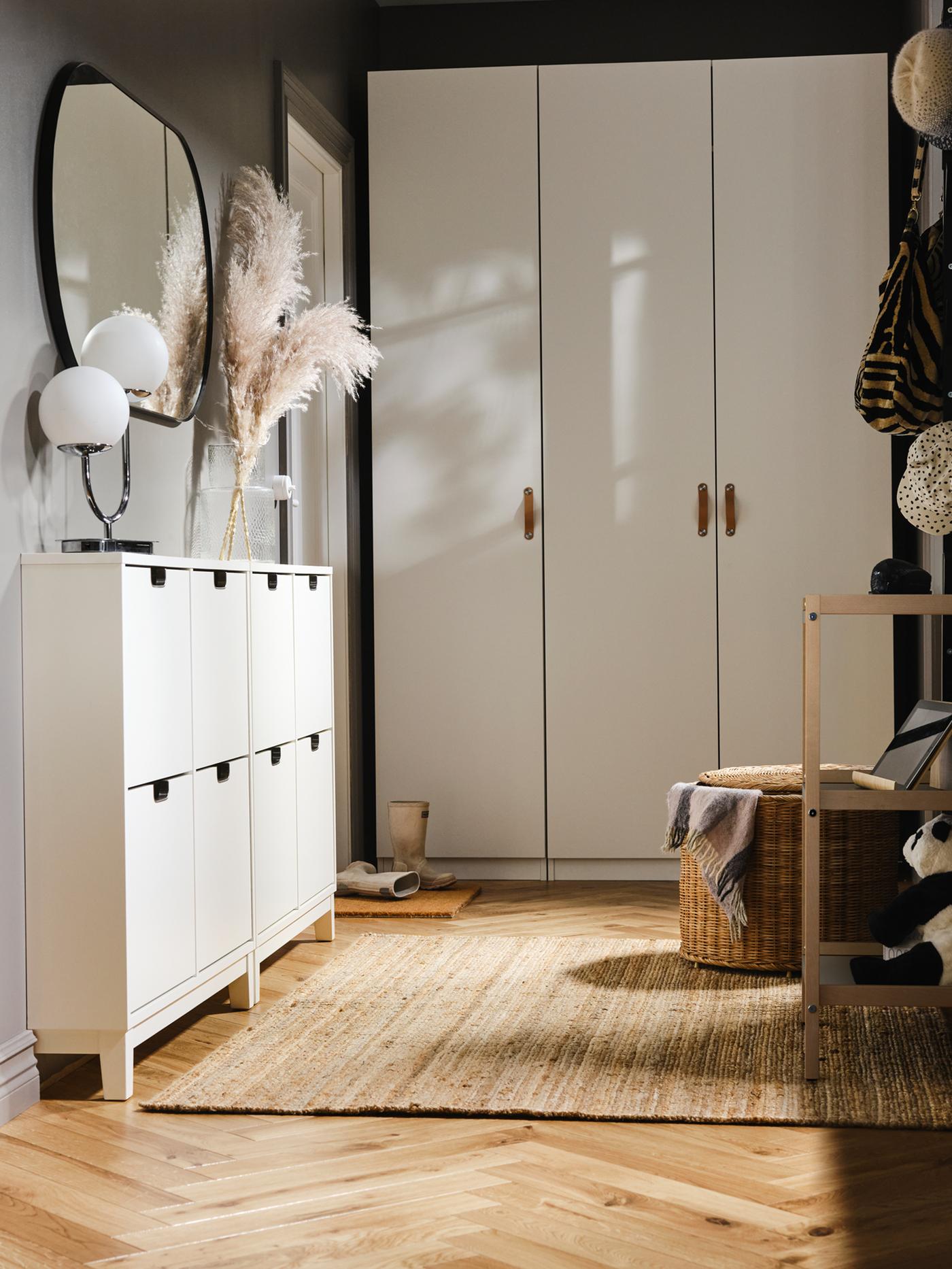 Am Ende eines Vorzimmers ist ein weißer PAX/FORSAND Kleiderschrank mit zwei weißen STÄLL Schuhschränken an einer Seite zu sehen. Über diesen hängt ein Spiegel.