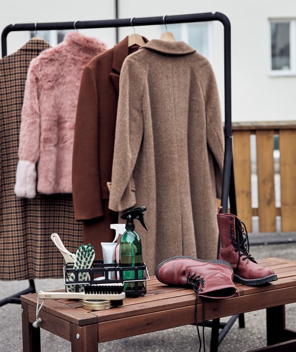 Ambiente exterior com um suporte para cabides TURBO com roupa de inverno pendurada, junto a um banco com um par de botas e um conjunto de limpeza.
