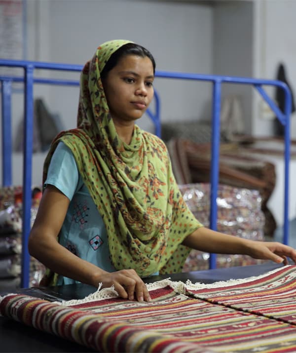 امرأة تحمل سجادة ملونة منقوشة على سطح عمل.