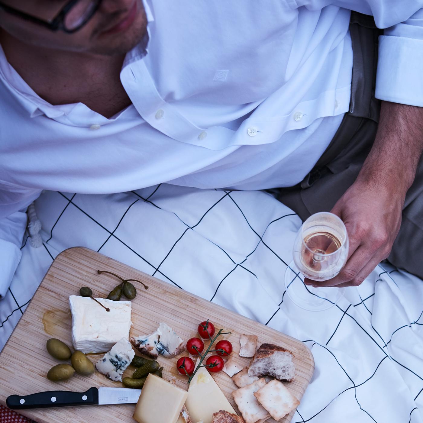 Amuse-bouche (fromages, olives et biscuits apéritifs) sur une planche à découper, le tout posé près d’un homme, sur une couverture.