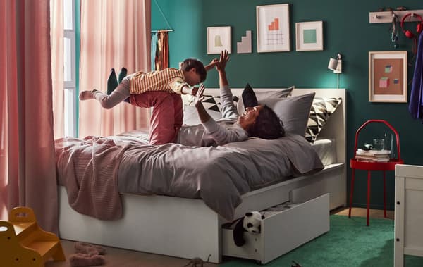 An adult and child playing on a queen bed with underbed storage drawers, with curtains hanging around the bed and artwork on the walls.