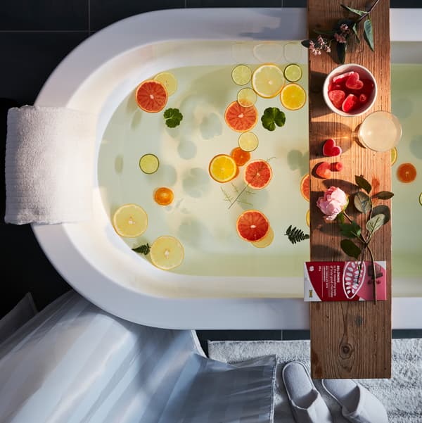 An aerial view of a bath filled with water and floating fruits, with a wooden shelf across which is covered with Valentine treats.