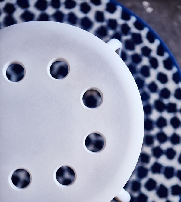 An aerial view of a circular stool with circle cut-outs on a circular black and white dotted rug.