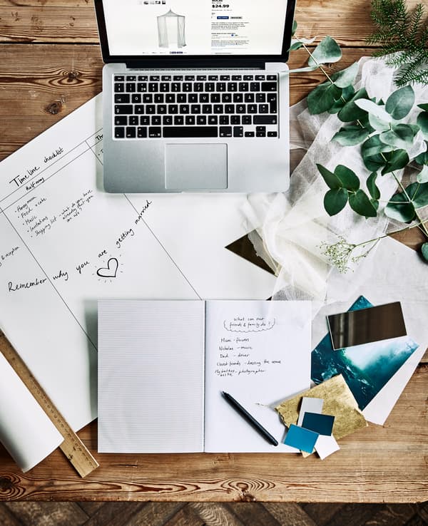 An aerial view of a desk with a computer, notebooks, a wedding planning timeline and fabric swatches