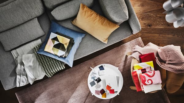 An aerial view of a grey sofa with different coloured cushions and blankets. A small table with fabric swatches sits nearby.