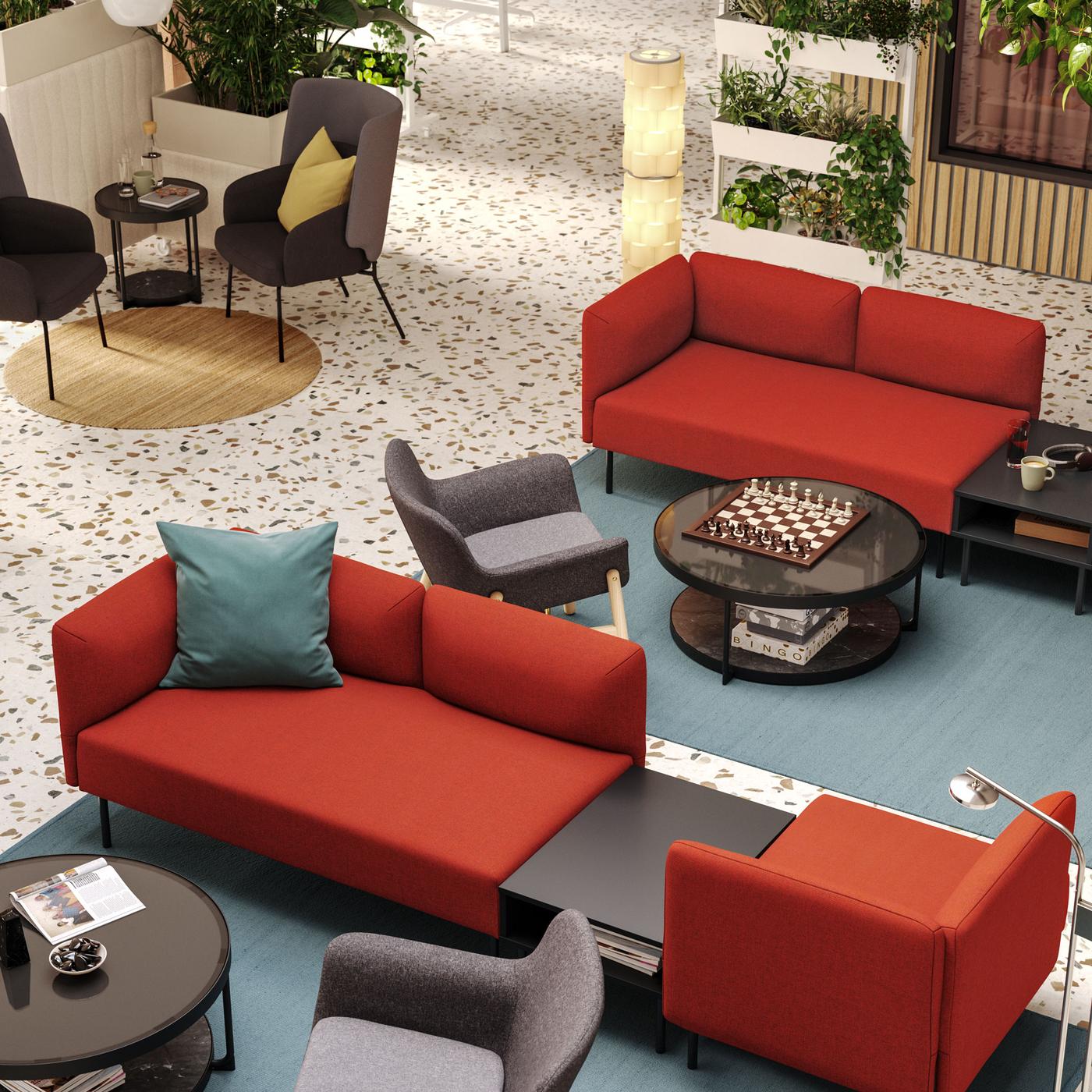 An aerial view of a hotel lobby with two seating areas defined by red LILLEHEM modular sofas and grey armchairs on big rugs.