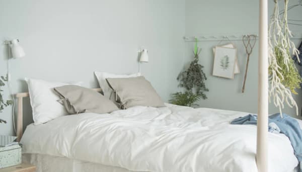 An aerial view of a symmetrical, green-walled bedroom with wood floors, green plants, low bedside tables and a large bed with a wooden frame 