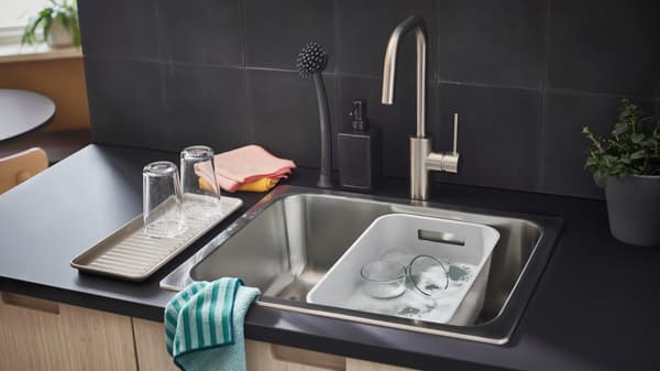An anthracite EKBACKEN countertop with a sink holding a grey GRUNDVATTNET washing-up bowl, microfiber cloths and accessories.