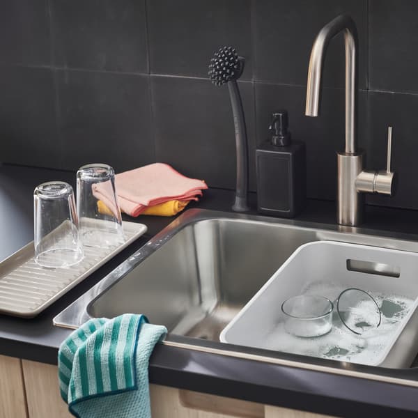 An anthracite EKBACKEN worktop with a sink holding a grey GRUNDVATTNET washing-up bowl, plus a pile of microfiber cloths.