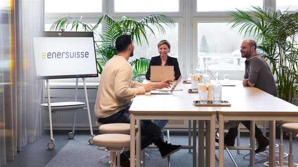 An area for presentations and meetings furnished with white desks where employees can either sit or stand. Three employees in a meeting. 