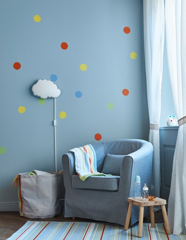  An armchair for nursing in a child’s room with blue walls and a cloud-shaped wall lamp.