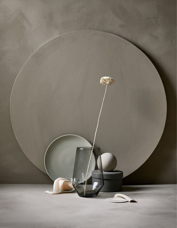 An arrangement of a glass vase and flower, plate, storage box and fabrics in similar colours.