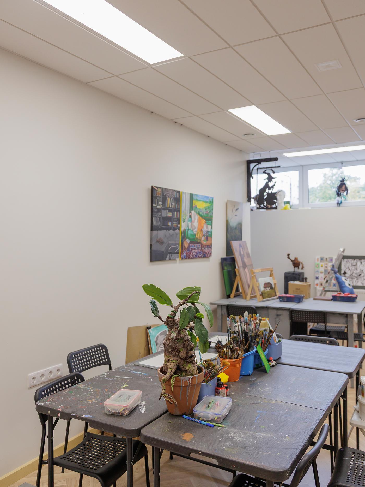 An art studio with a large table surrounded by chairs, showing signs of wear before renovation.