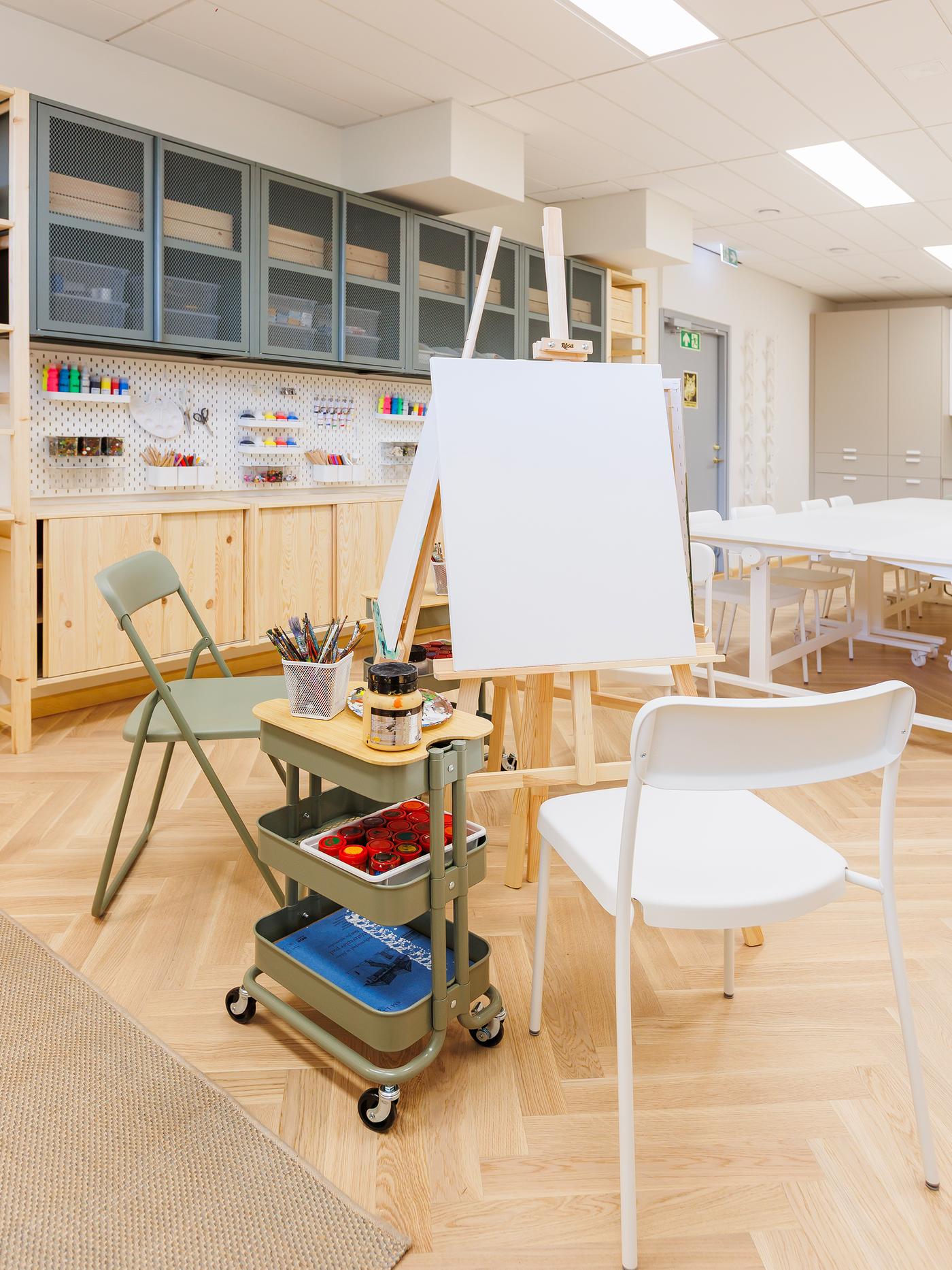 An art studio workspace with folding chairs, an easel and art supplies on a trolley.